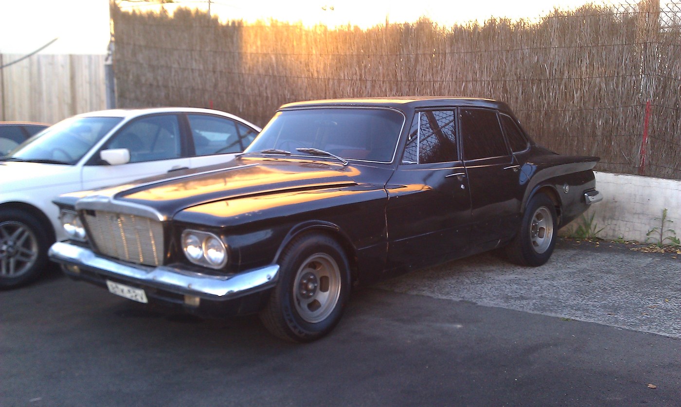 Original snapshot of a vintage black sedan parked next to a fence