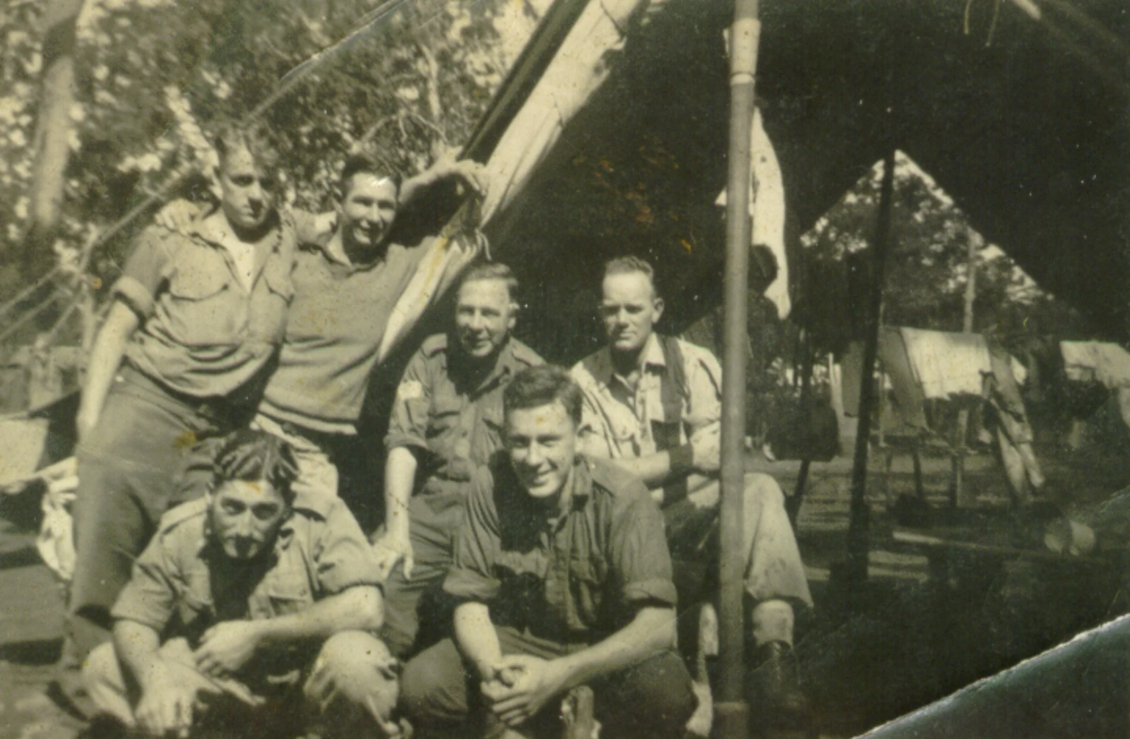 Damaged black-and-white WWII-era photograph of a group of soldiers smiling outside a tent