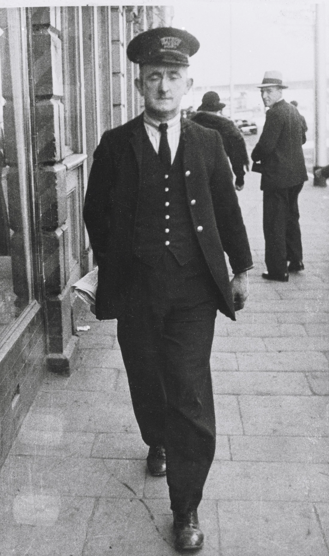 Damaged vintage photograph of a 1940s traffic warden walking down a city street